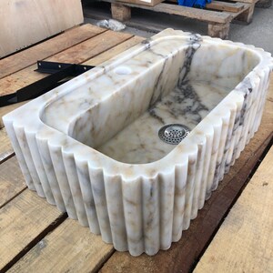 calacatta viola marble sink, fluted marble sink, grooved marble sink, wall mounted marble sink, wall hung stone basin, small powder room sink, compact bathroom sink, luxury powder room vanity, handcrafted marble basin, natural stone bathroom sink, custom marble sink, purple marble sink, burgundy marble sink, floating marble vanity, designer bathroom sink, boutique hotel bathroom sink, narrow bathroom sink, handmade stone sink, marble washbasin, architectural bathroom sink