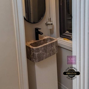 May include: A brown marble pedestal sink with a black faucet and a white soap dispenser. The sink is in a small bathroom with a white wall and a window.