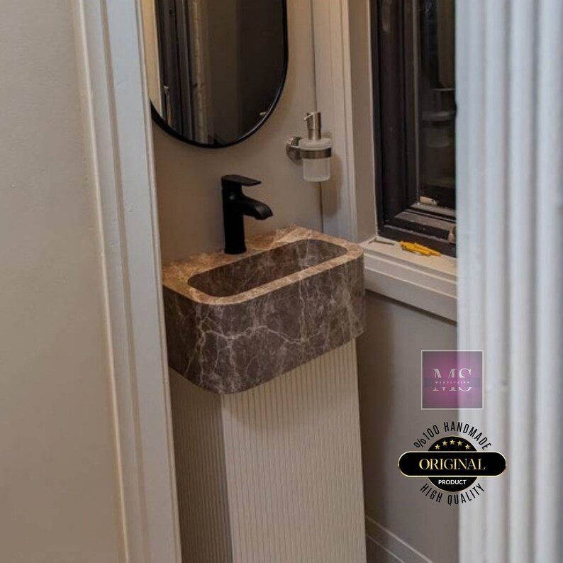 May include: A brown marble pedestal sink with a black faucet and a white soap dispenser. The sink is in a small bathroom with a white wall and a window.