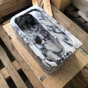 May include: A white marble sink with purple veining. The sink has two basins and a single drain hole. The sink is sitting on a wooden pallet.