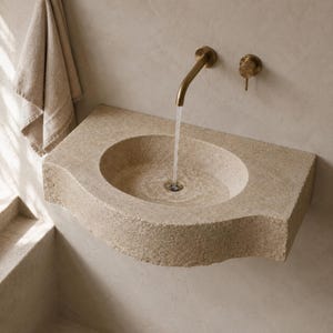 Wall-mounted travertine basin with water flowing from an aged brass wall faucet