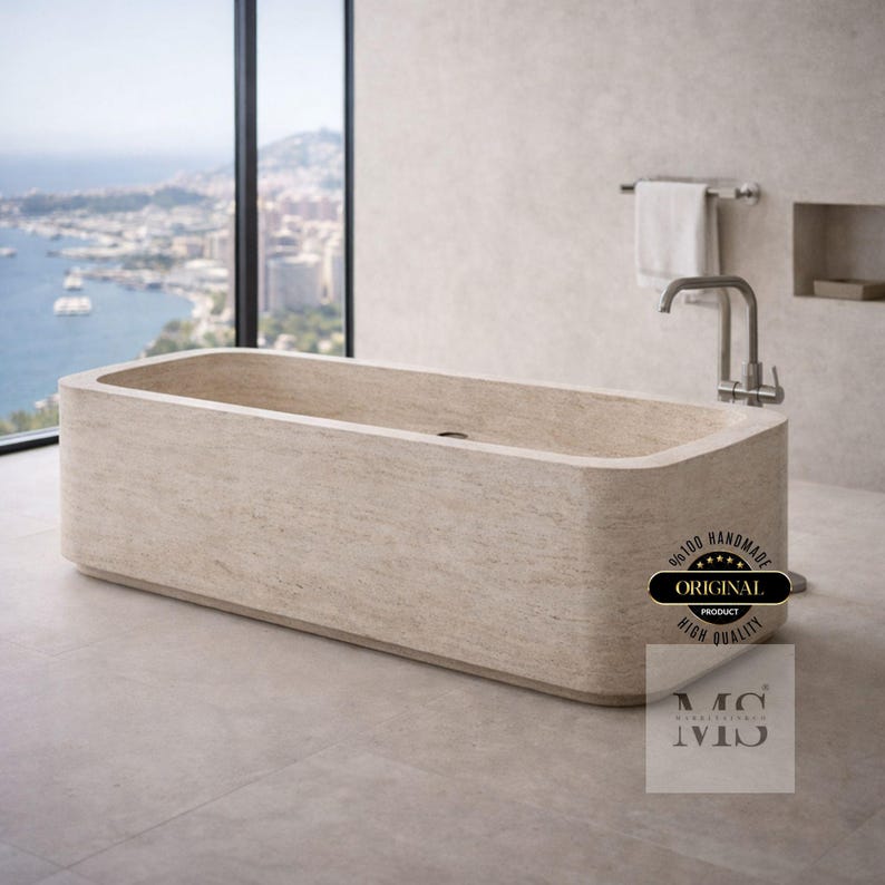 May include: A rectangular, beige stone bathtub with rounded edges. A chrome faucet and towel rack are mounted on the wall. The image includes a window with a view of a coastal city and the text "ORIGINAL PRODUCT HIGH QUALITY".