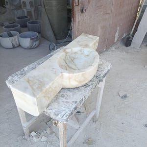Luxurious wall-mounted Calacatta marble sink carved from a single block. Featuring 3 faucet holes, fluted front design, and floating vanity look. Ideal for modern, minimalist bathrooms. Custom sizes available. Handmade from natural Italian stone. Bathroom sink, marble vanity, stone basin, designer sink, fluted marble, wall mount sink, handmade sink, rectangular sink, luxury bathroom decor.