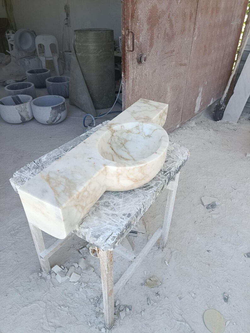Luxurious wall-mounted Calacatta marble sink carved from a single block. Featuring 3 faucet holes, fluted front design, and floating vanity look. Ideal for modern, minimalist bathrooms. Custom sizes available. Handmade from natural Italian stone. Bathroom sink, marble vanity, stone basin, designer sink, fluted marble, wall mount sink, handmade sink, rectangular sink, luxury bathroom decor.