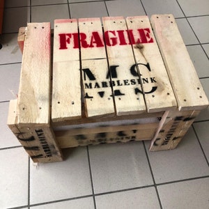 May include: A wooden crate with the word "FRAGILE" printed in red letters. The crate is labeled with the text "MARBLESINK" in black letters.