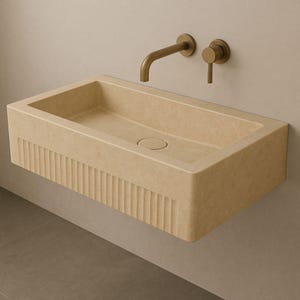 Handmade travertine wall-mounted sink with fluted front and matte finish. Custom sizes available. Ideal for luxury bathrooms, hotels, interior designers, and modern spa spaces. Each basin is carved from solid stone. Ships globally in a wooden crate via DHL Express. Natural veining varies uniquely in each piece.Perfect for minimalist,rustic,and architectural interiors, travertine wall-mounted sink,fluted front, solid stone, custom sizes,interior designers, modern spa, luxury bathrooms, minimalist