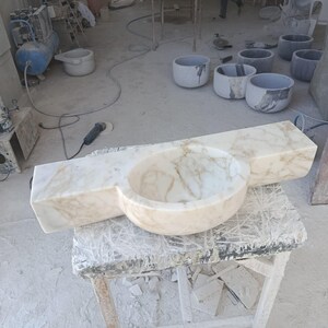 Luxurious wall-mounted Calacatta marble sink carved from a single block. Featuring 3 faucet holes, fluted front design, and floating vanity look. Ideal for modern, minimalist bathrooms. Custom sizes available. Handmade from natural Italian stone. Bathroom sink, marble vanity, stone basin, designer sink, fluted marble, wall mount sink, handmade sink, rectangular sink, luxury bathroom decor.