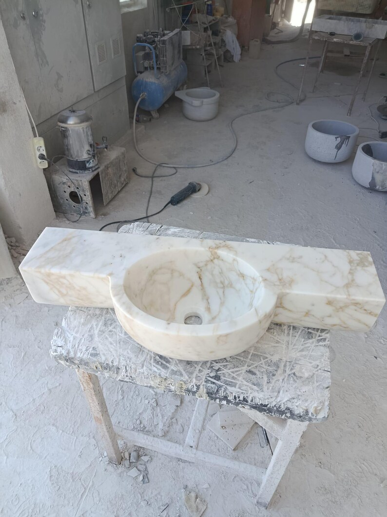 Luxurious wall-mounted Calacatta marble sink carved from a single block. Featuring 3 faucet holes, fluted front design, and floating vanity look. Ideal for modern, minimalist bathrooms. Custom sizes available. Handmade from natural Italian stone. Bathroom sink, marble vanity, stone basin, designer sink, fluted marble, wall mount sink, handmade sink, rectangular sink, luxury bathroom decor.