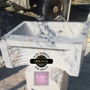 May include: A white marble sink with a unique, wavy design. The sink is handmade and features a label that reads "9/100 Handmade Original Product High Quality".