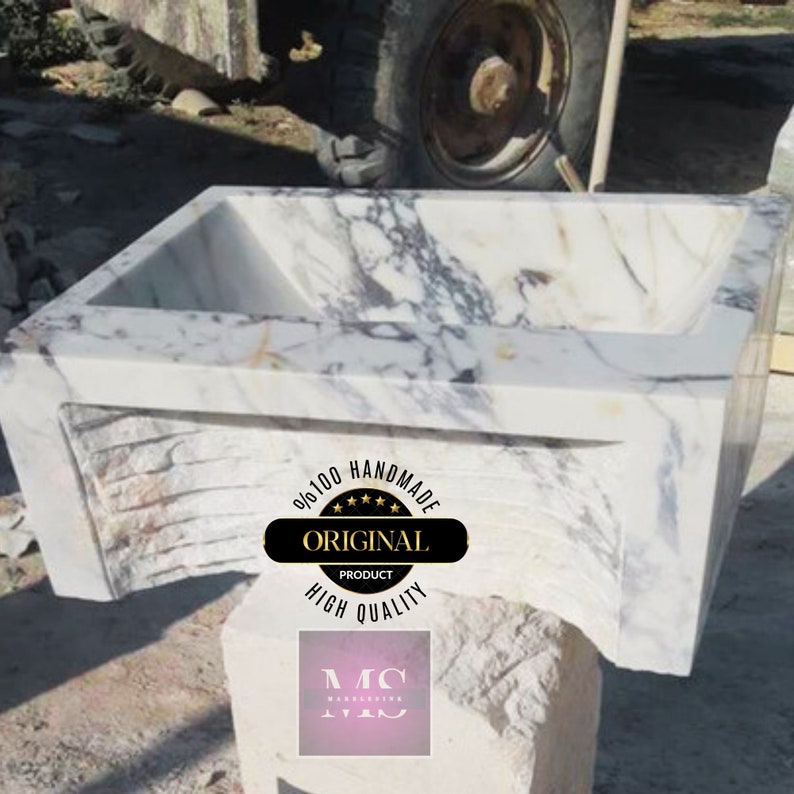 May include: A white marble sink with a unique, wavy design. The sink is handmade and features a label that reads "9/100 Handmade Original Product High Quality".
