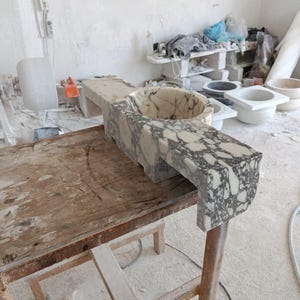 Luxurious wall-mounted Calacatta marble sink carved from a single block. Featuring 3 faucet holes, fluted front design, and floating vanity look. Ideal for modern, minimalist bathrooms. Custom sizes available. Handmade from natural Italian stone. Bathroom sink, marble vanity, stone basin, designer sink, fluted marble, wall mount sink, handmade sink, rectangular sink, luxury bathroom decor.