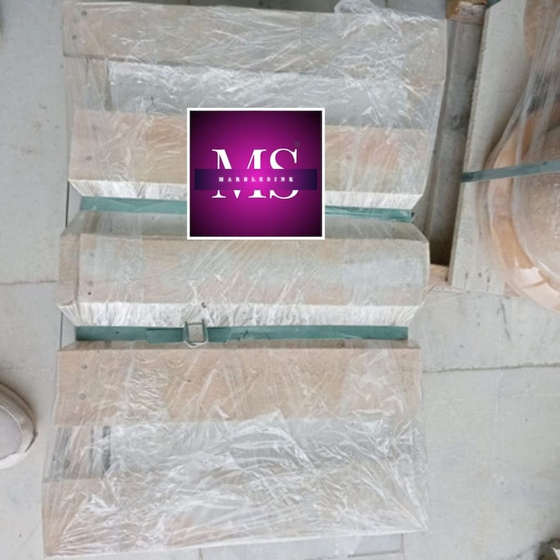 May include: Three wooden planks wrapped in clear plastic, stacked on top of each other. The planks are secured with a green strap and a metal buckle. The planks are labeled with the text "MS MARBLERINK".