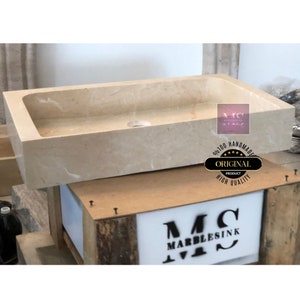 May include: A rectangular stone sink with a smooth, light beige surface. The sink is sitting on a wooden crate with a white label that says "MC MARBLESINK".