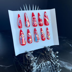 Könnte beinhalten: Set mit 10 roten Press-on-Nägeln mit holografischem Finish. Jeder Nagel hat ein anderes Design, darunter Totenköpfe, Herzen und abstrakte Formen.