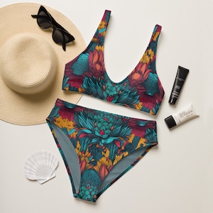 May include: A two-piece bikini set with a vibrant floral pattern in teal, burgundy, and yellow. The bikini top has a scoop neck, and the high-waisted bottoms are also patterned. A straw hat, sunglasses, sunscreen, and a seashell are also in the image.