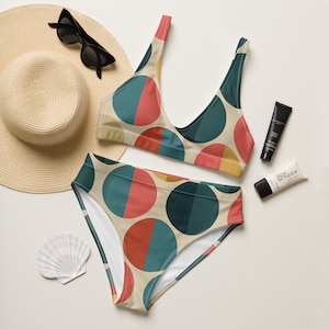 May include: A two-piece bikini set with a beige background and a pattern of large, colorful half-circles in teal, red, and yellow. The set is accompanied by a straw hat, sunglasses, sunscreen, and a seashell.