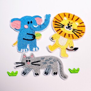May include: Embroidered patches of a blue elephant with pink ears, a yellow lion with a brown mane, and a grey cat. The patches are in a cartoon style with white borders and small green grass accents.