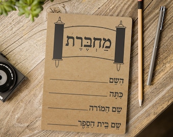 Puede incluir: Una libreta marrón con una ilustración en blanco y negro de un rollo de la Torá con la palabra hebrea "Mahberet" que significa "libreta". La libreta tiene líneas para escribir.