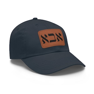 May include: Navy blue baseball cap with a brown leather patch. The patch features black Hebrew text. A classic, adjustable hat for everyday wear.