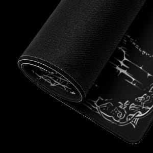 May include: Rolled-up black mouse pad with white stitched edges. The pad features a detailed white graphic design on the visible surface. The texture of the pad is visible, and the background is black.