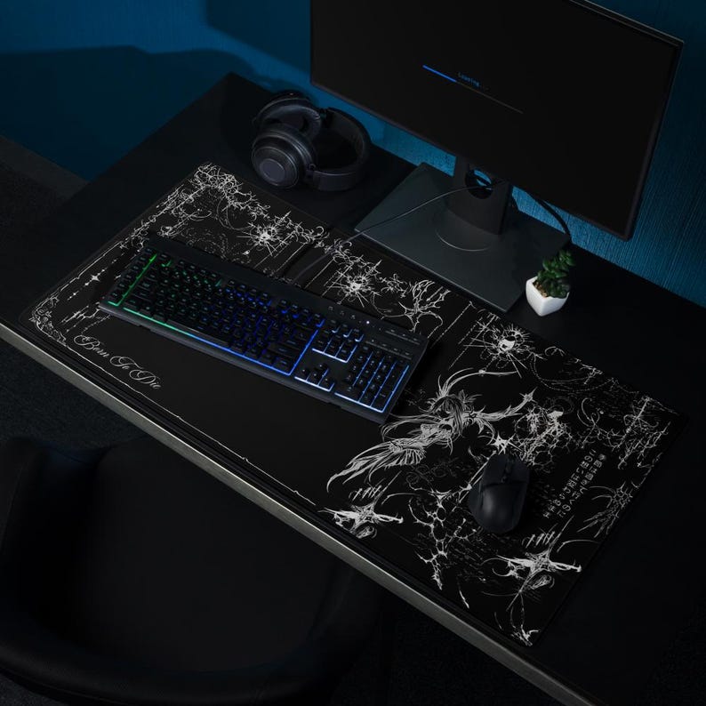 May include: Black gaming desk setup with a keyboard, mouse, and two mousepads. The mousepads have a white graphic design and the text "Born To Die" and Japanese text. A monitor, headphones, and a small plant are also on the desk.