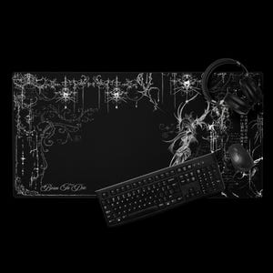 May include: Black gaming mouse pad with white decorative floral and gothic-style illustrations. The words "Born To Die" are printed on the pad. A black keyboard, mouse, and headphones are also visible.