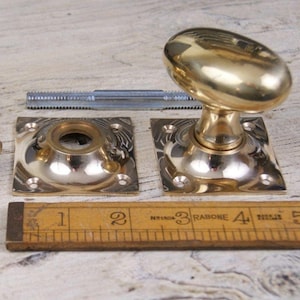 May include: A set of antique brass door knobs with square backplates and a tap. The knobs have an oval shape. A wooden ruler shows measurements in centimetres.