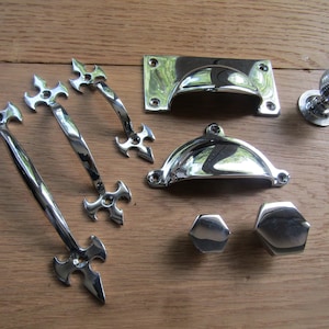 Puede incluir: Un juego de ocho piezas de herrajes para armarios de cromo pulido, que incluyen tres tiradores de puerta ornamentados, dos tiradores de taza, una perilla y dos perillas pequeñas.