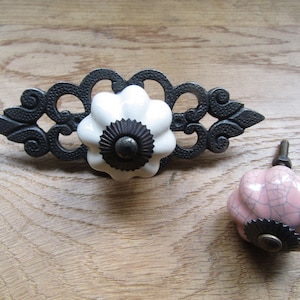 May include: Two ceramic drawer pulls with a black metal base. The top pull is white with a black centre and the bottom pull is pink with a black centre.