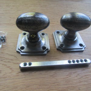 May include: Two silver oval door knobs with square backplates and a silver metal bar.