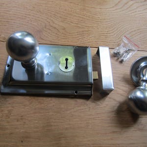 May include: A polished chrome door lock set with a rectangular latch, two round door knobs, and a keyhole. The set is laid out on a wooden surface.