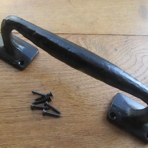 以下が含まれることがあります： 黒色の鍛鉄製ドアプル。曲線的なハンドルと2つの長方形の取り付けプレートがあります。黒いネジの小さな山が含まれています。このハードウェアは、素朴または農家の美学のために設計されています。