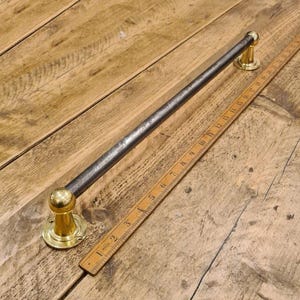 May include: A metal towel bar with brass-colored end mounts. The bar is dark gray and has a slightly textured surface. A wooden ruler is next to the bar, showing measurements in inches.