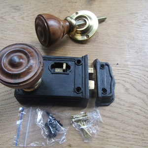May include: A vintage door knob set with a dark brown wooden knob and brass detailing, a black metal latch, and fixings. The set includes a matching knob and a separate latch mechanism, suitable for restoration projects. The knob measures approximately 7 cm in diameter.