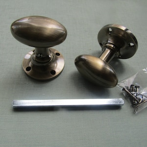 Puede incluir: Dos pomos de puerta ovalados de latón antiguo con placas traseras redondas y tornillos.