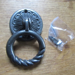 May include: A dark grey metal drawer pull with a decorative floral backplate and a twisted ring handle. Includes screws in a small plastic bag. Suitable for furniture restoration or adding a rustic touch.