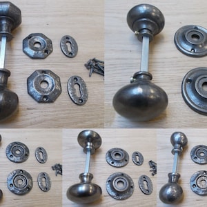 May include: Set of four antique-style door knobs with different designs. Each knob is made of metal and has a dark gray finish. The knobs come with matching plates and screws.