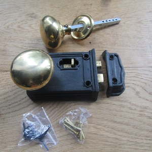 Może przedstawiać: Zamek do drzwi z czarnego żeliwa z mosiężną gałką i oddzielną płytką zatrzaskową. Zamek jest przeznaczony do drzwi z zamkiem wpuszczanym. Zestaw zawiera śruby do montażu.