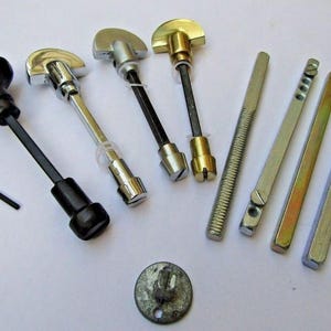 May include: Assortment of metal door knobs and handles in silver and gold tones. The set includes a black knob, a round knob, and several long, thin pieces of metal.