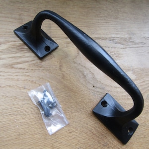 May include: Black metal door handle with a curved design. The handle is attached to a rectangular plate with two screws. The handle comes with a small bag of screws.