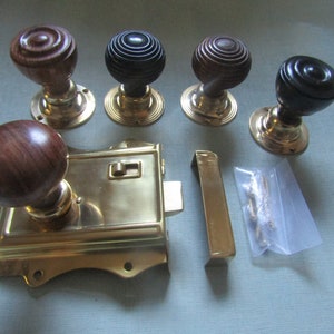 Pode incluir: Um conjunto de ferragens de porta antigas, incluindo vários puxadores de porta de madeira com bases de latão, uma fechadura de porta de latão e uma placa de fecho. Os puxadores têm diferentes acabamentos em madeira.