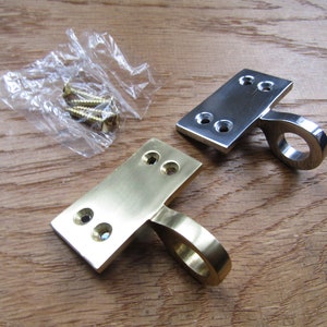 Puede incluir: Dos pestillos para puertas o ventanas, uno en latón pulido y otro en níquel pulido. Cada pestillo tiene una base rectangular con dos agujeros para tornillos y una manija de bucle redondeada.