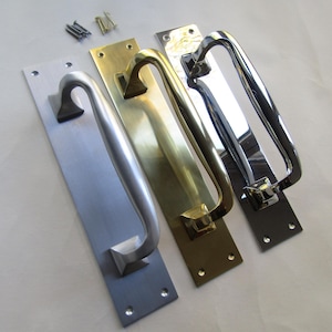 May include: A selection of door pull handles in various finishes: brushed nickel, brass, and polished chrome. Each handle is mounted on a rectangular backplate with screw holes, and includes mounting hardware.