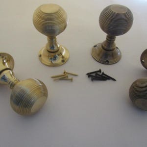 Op de afbeelding: Vier antieke messing deurknopjes met een geribbeld ontwerp. De knoppen worden getoond op een wit oppervlak met schroeven.