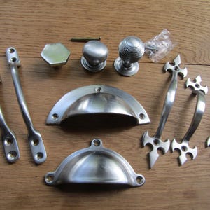 Può includere: Una collezione di ferramenta per armadi color argento, tra cui pomelli, maniglie e maniglie per cassetti. La ferramenta presenta una varietà di stili, tra cui rotondi, quadrati e decorativi.