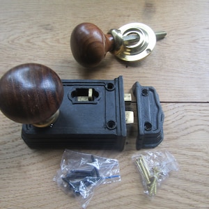 May include: A black cast iron door lock with two wooden knobs, a brass escutcheon, and a set of screws. The lock is in two pieces, with the latch separate from the main body.