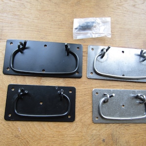 Könnte beinhalten: Vier Schubladengriffe, zwei schwarz und zwei silber, mit einem einfachen, abgerundeten rechteckigen Design. Die Griffe werden auf einer Holzoberfläche gezeigt.