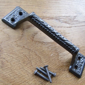 May include: A cast iron door handle with an ornate design. The handle is black and has a textured finish. It comes with four screws for installation.