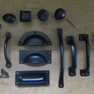 Könnte beinhalten: Eine Sammlung von schwarzen Metall-Schrankbeschlägen, darunter Schubladenzüge, Türgriffe und Knöpfe. Die Beschläge haben eine rustikale, antike Oberfläche.