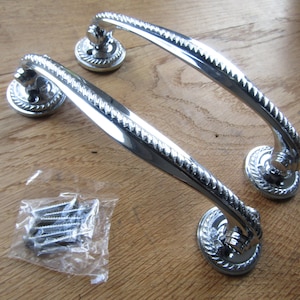 May include: Two silver door handles with a rope design and a round base. The handles are on a wooden surface and come with screws.